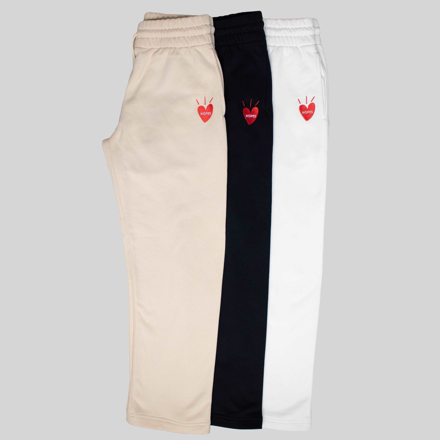 Product shot of Hopesbrands Big Heart sweatpants in black, off-white, and tan. Each pair features the embroidered Big Heart logo on the right thigh, made from a soft cotton blend for stylish, comfortable, everyday wear.