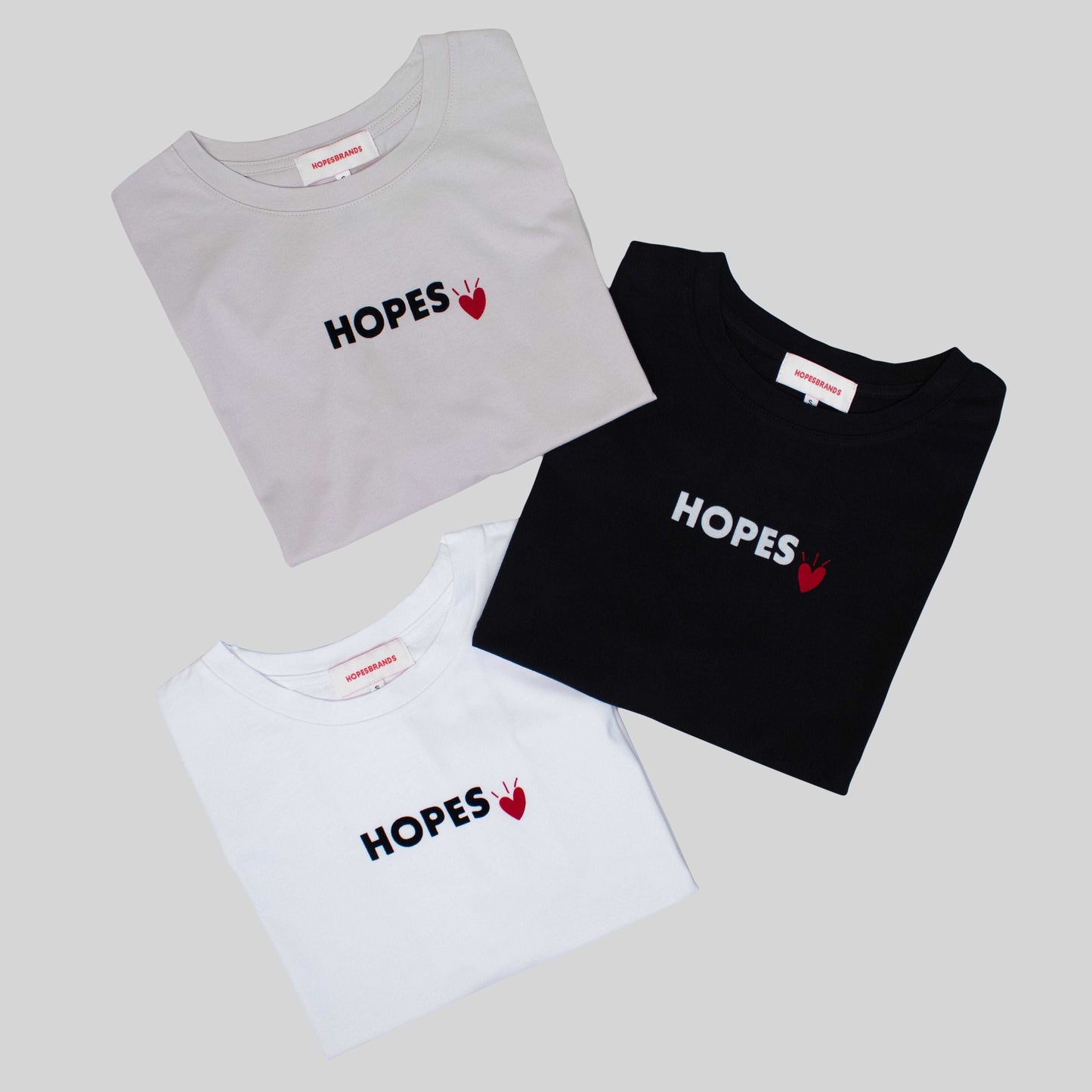 Product shot of Hopesbrands women's oversized Cool Touch T-shirts in black, white, and beige. The black T-shirt features a white Hopes logo with a red heart, while the others have the logo in black.
