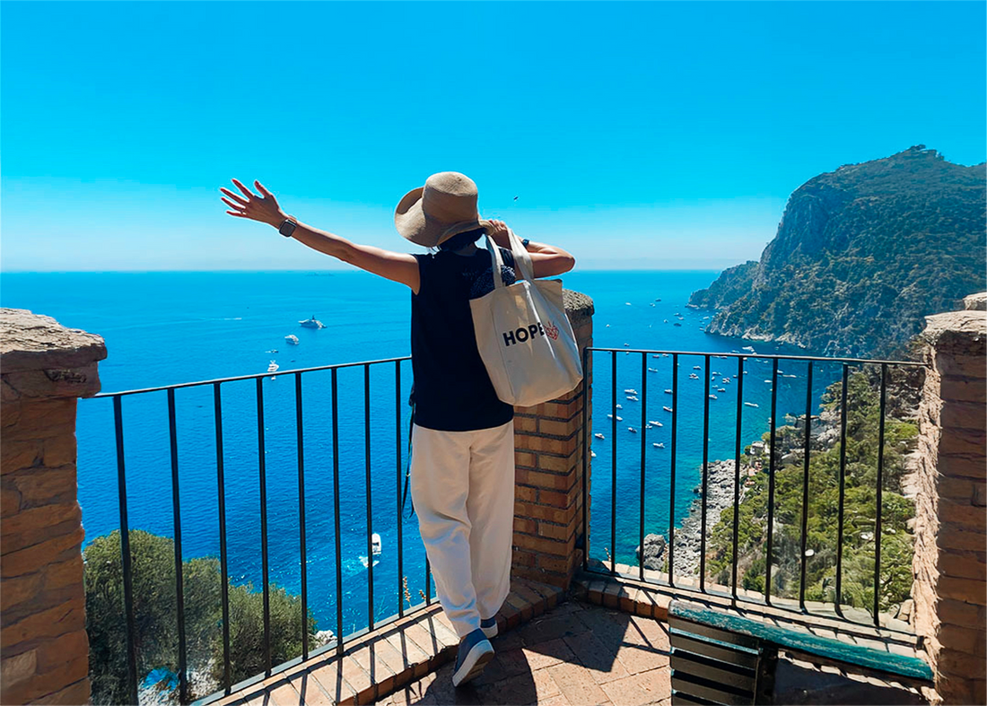 Female entrepreneur carry Hopes tote bag with arms outstretched overlooking Mediterranean sea during business break