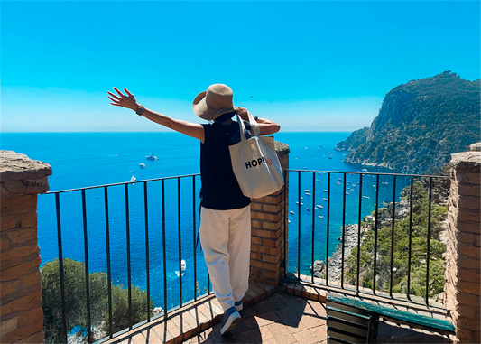 Female entrepreneur carry Hopes tote bag with arms outstretched overlooking Mediterranean sea during business break